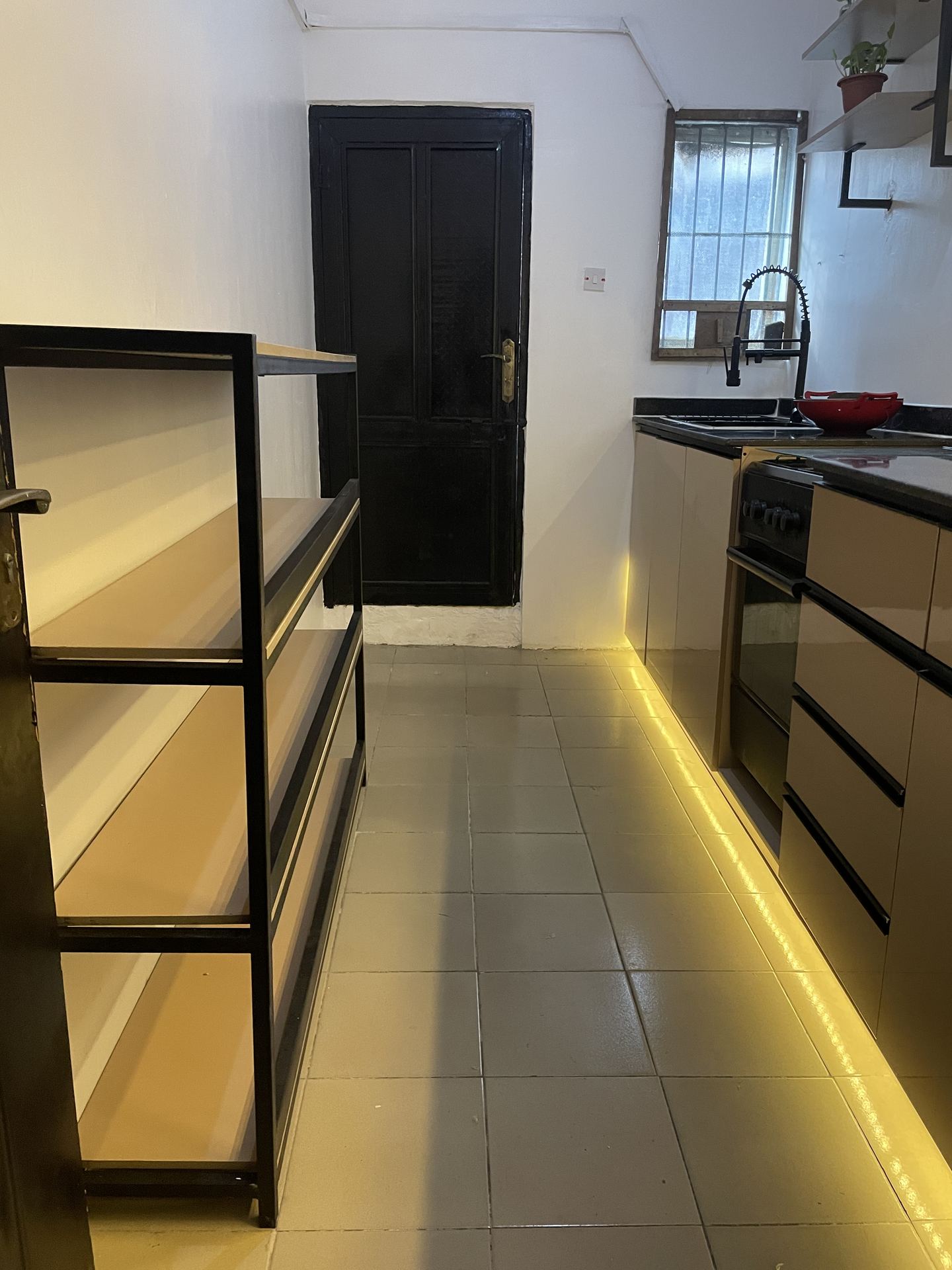 Full galley view with central shelving, dark worktops and warm floor lighting