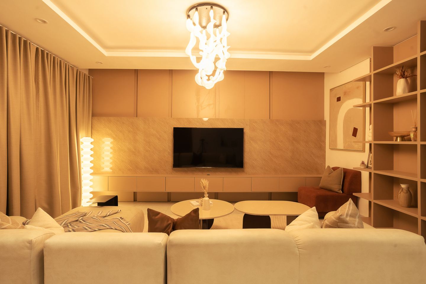 The living room: a sectional sofa facing the screen set into a panelled wall, under a sculptural pendant