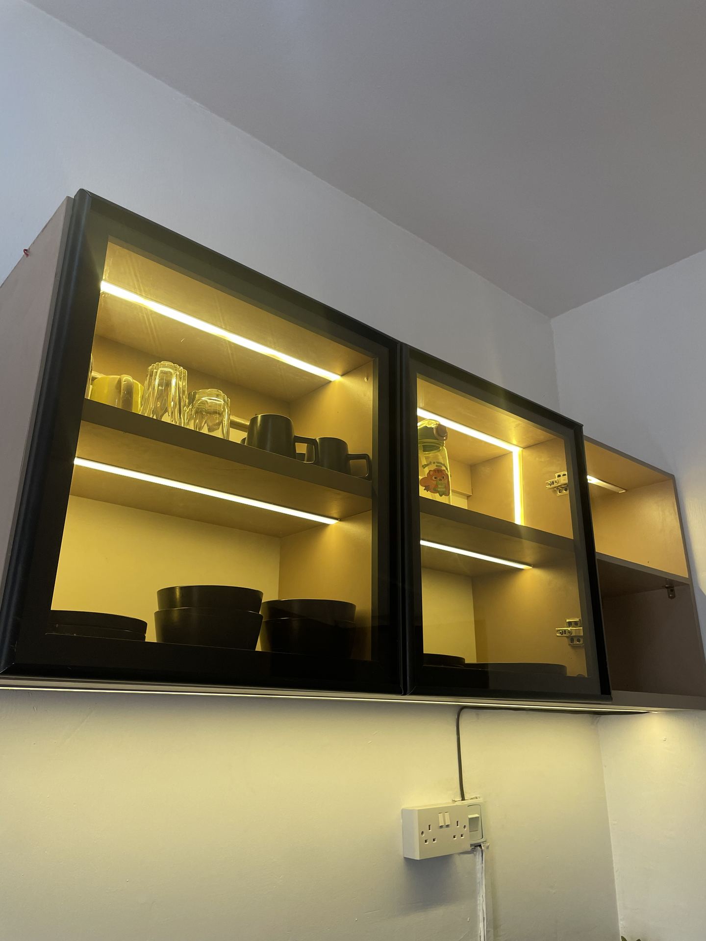 Warm-lit glass-front wall cabinets above the kitchen worktop