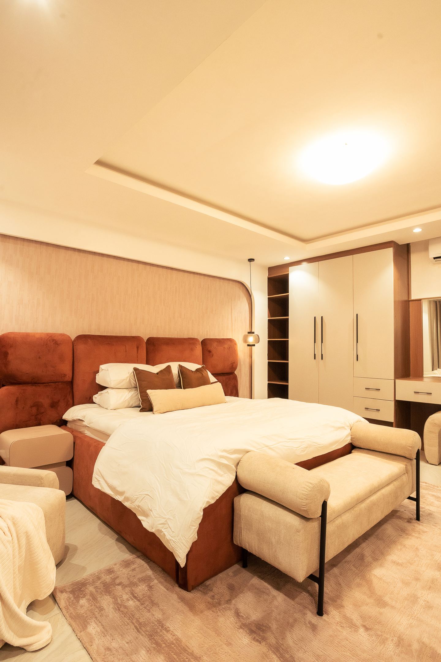 A bedroom with a rust velvet headboard beside fitted wardrobes