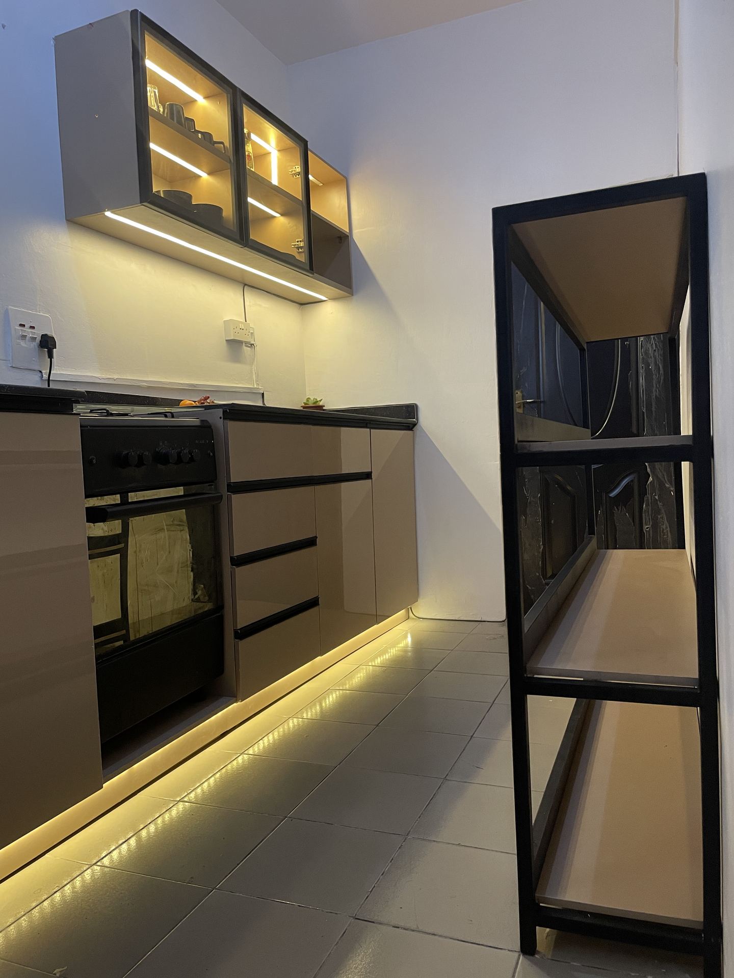 Wide kitchen counter with black sink, taupe drawers and lit cabinetry