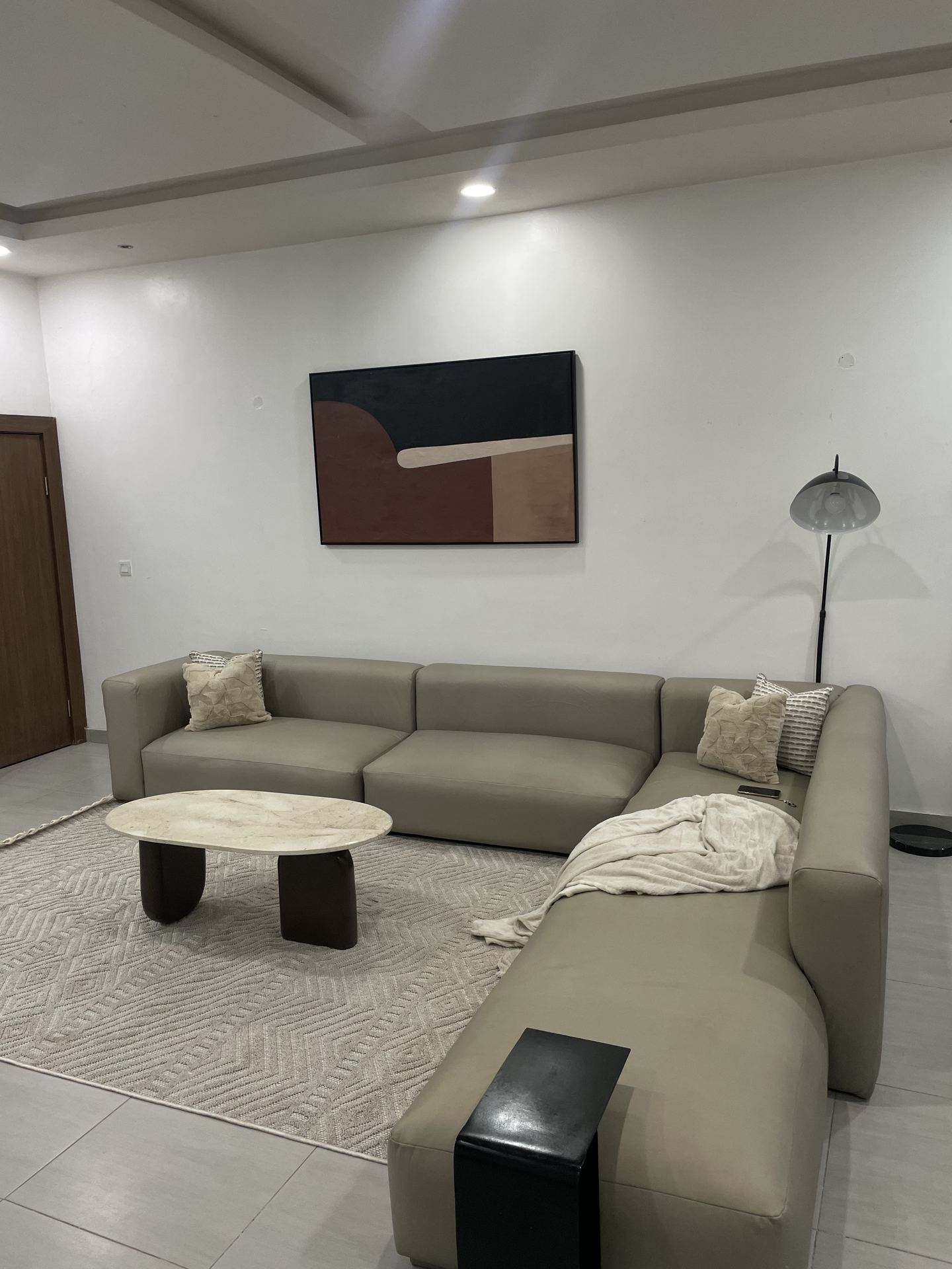 Neutral sectional sofa beneath abstract artwork and an arched floor lamp
