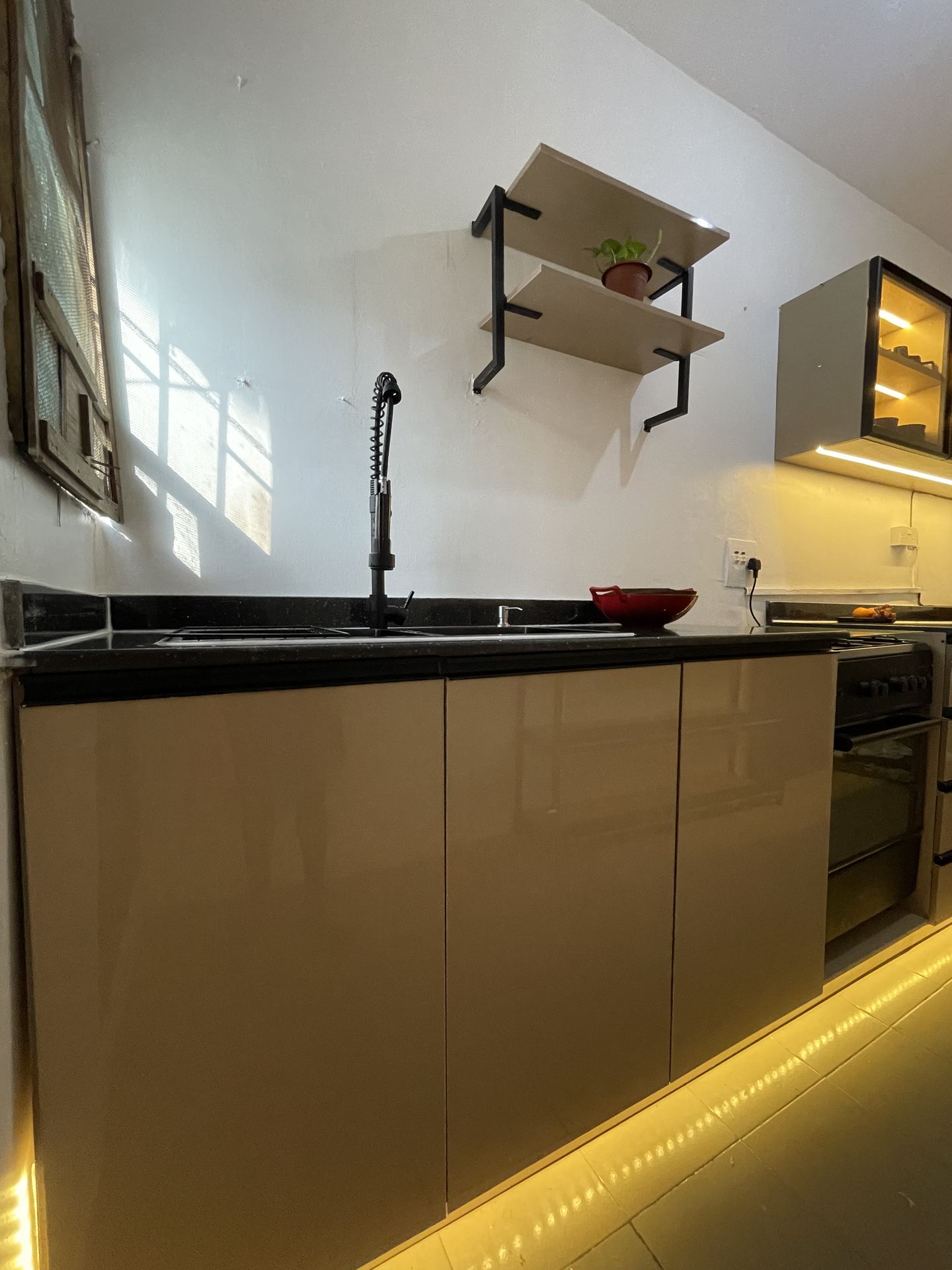 Kitchen sink run with warm under-cabinet lighting and open shelf