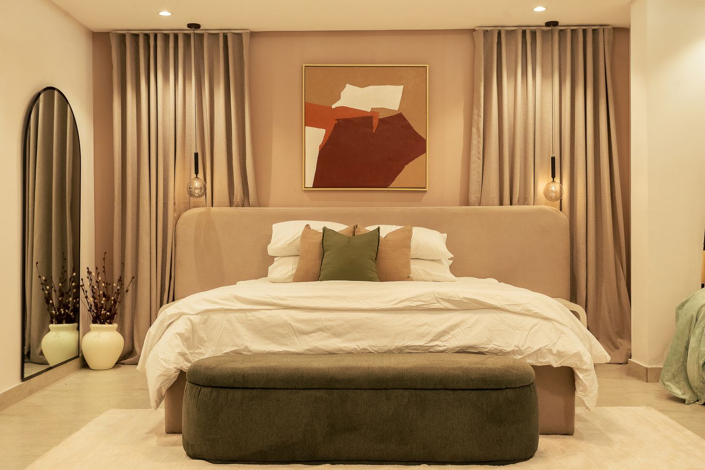 A bedroom with an arched mirror and a long bench at the foot of the bed