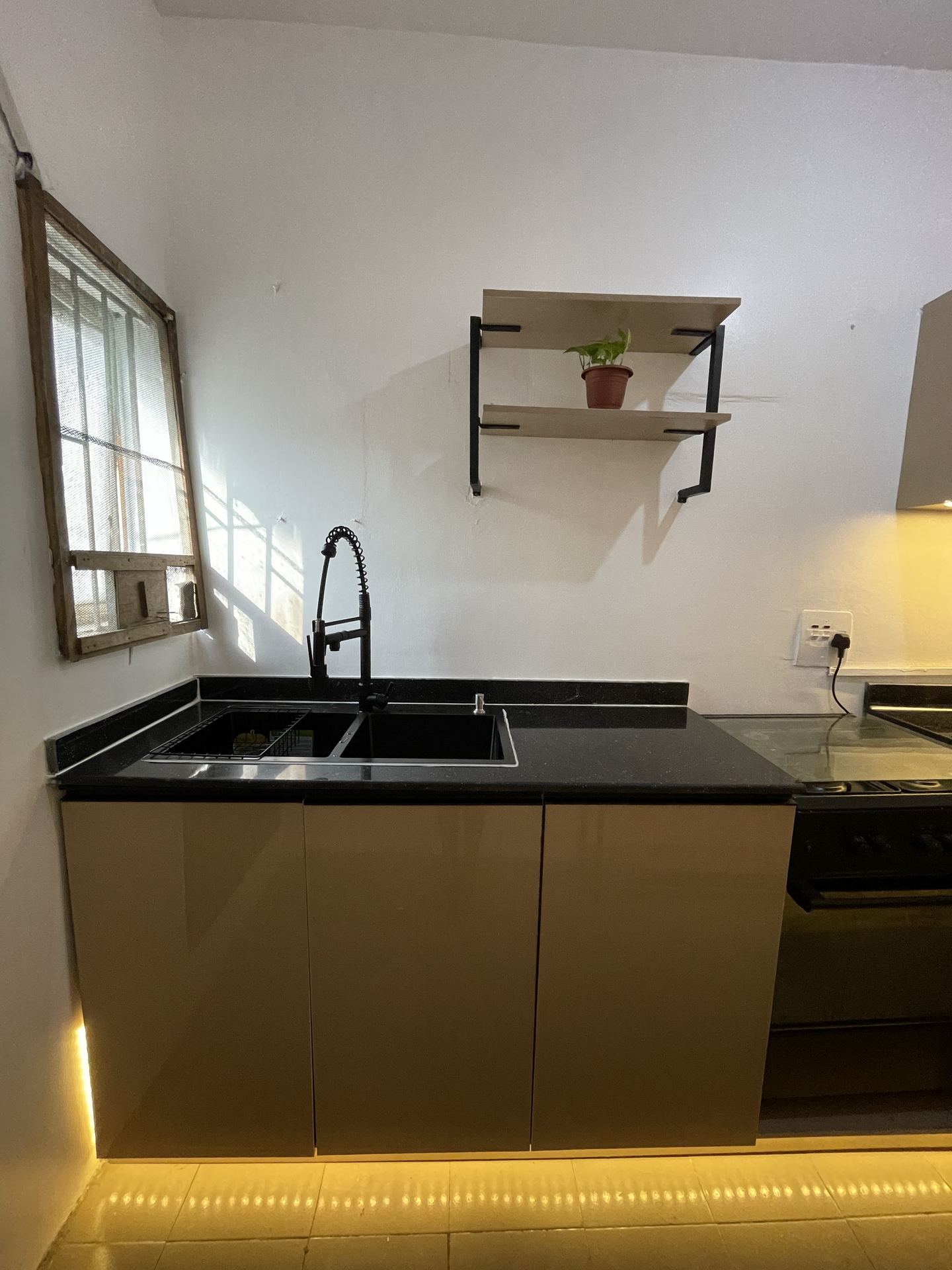 Sunlit black sink and spring faucet beneath a floating wall shelf
