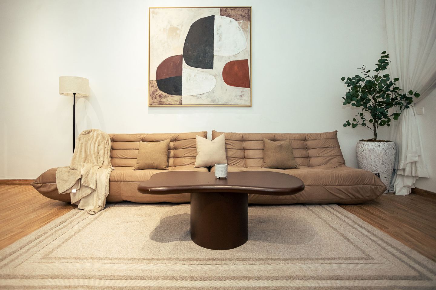 A sitting room: a low tufted sofa, a dark round table and one large canvas
