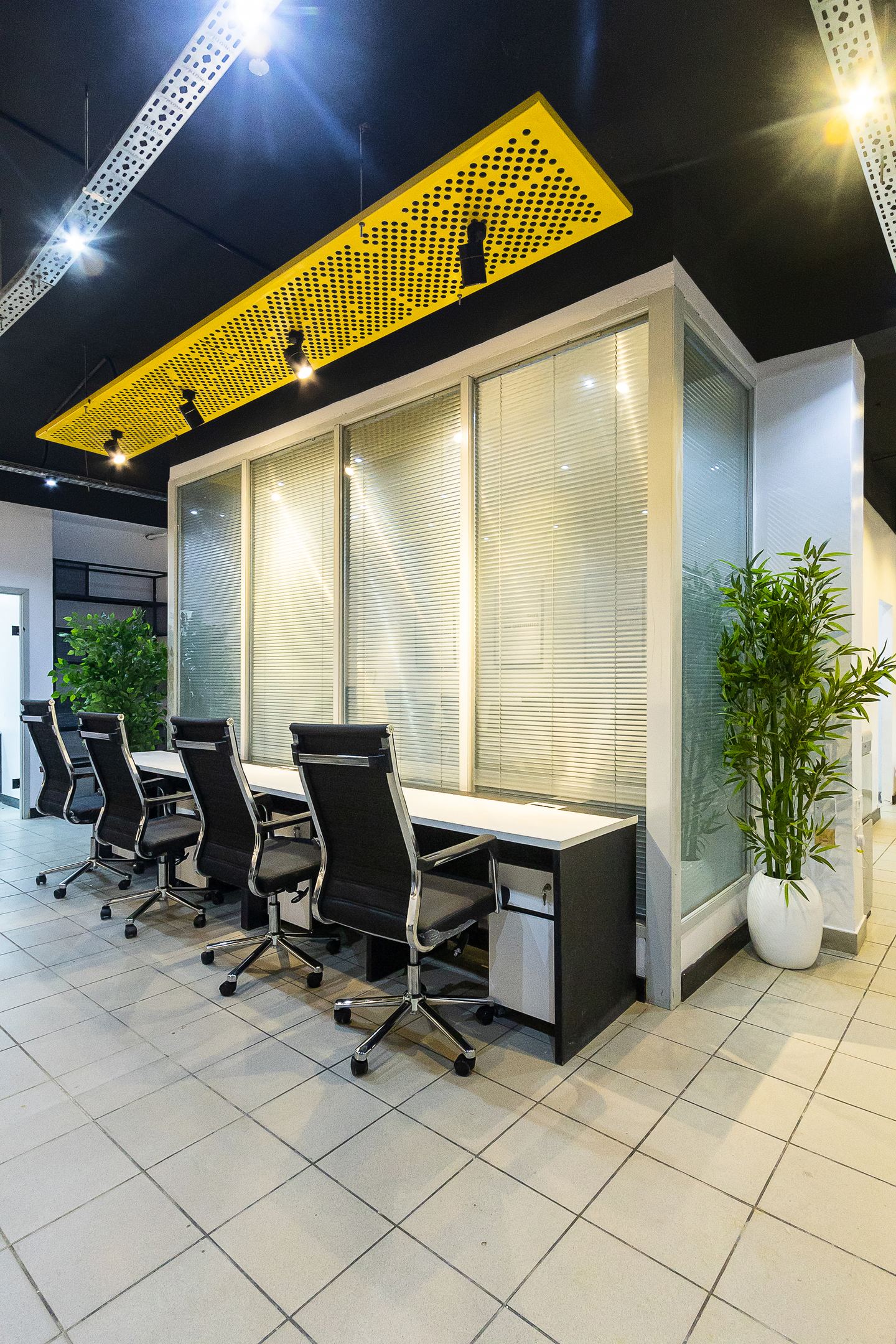 Desks along the glazed partition, under a yellow perforated raft